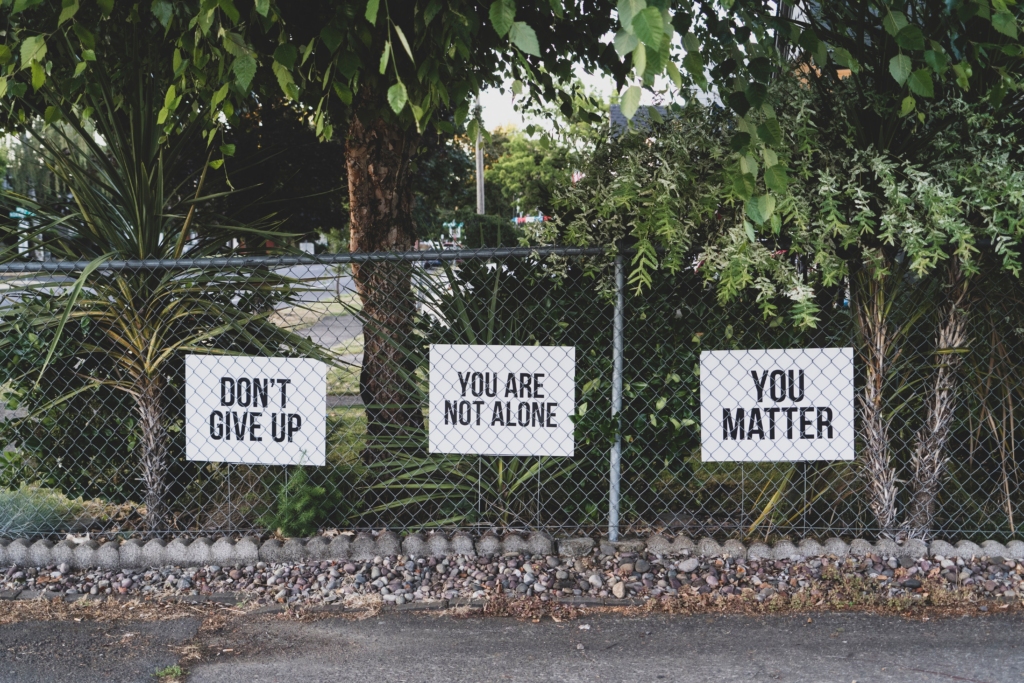 A picture of garden, and behind the fence are three signs with Don't Give Up, You are Not Alone, and You Matter on them.