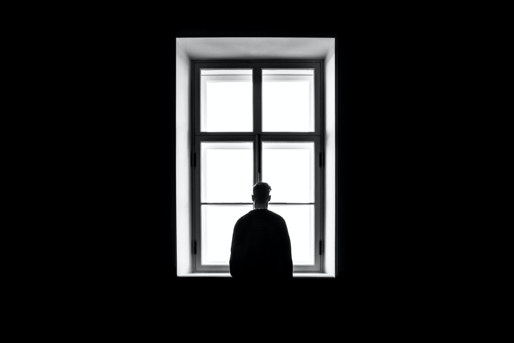 A monochrome image of a solitary man staring through a window