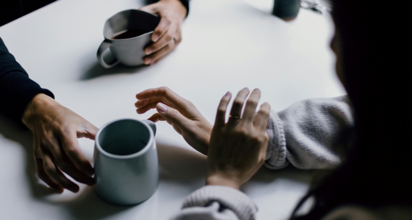 Couple sitting across from each other, holding hands, with two ceramic mugs on the table between them