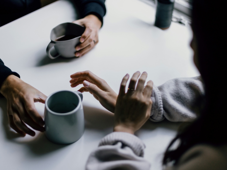 Couple sitting across from each other, holding hands, with two ceramic mugs on the table between them