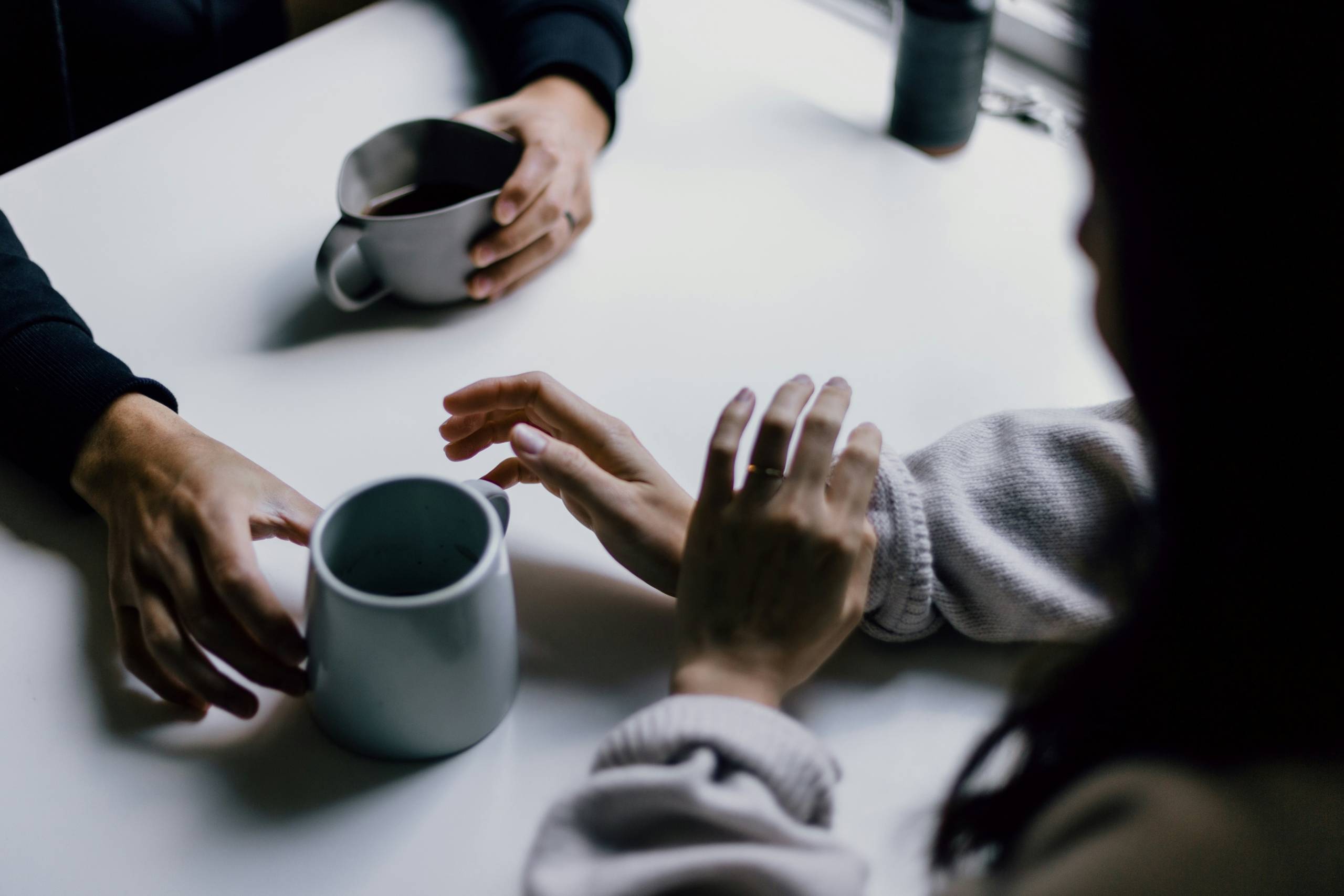 Couple sitting across from each other, holding hands, with two ceramic mugs on the table between them